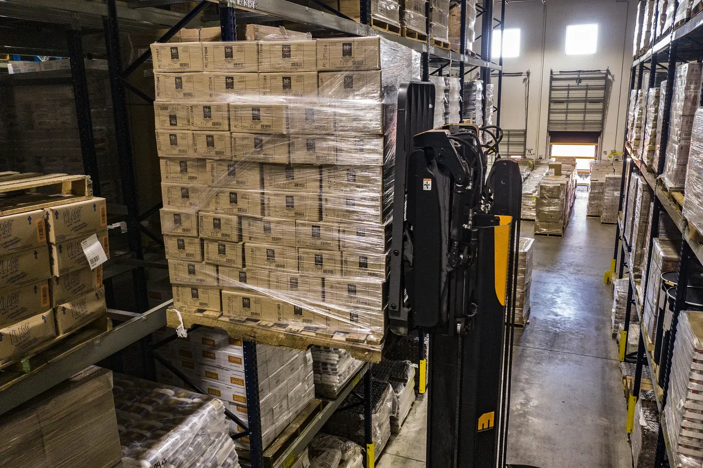 Forklift lifting a wrapped pallet of cartons in a warehouse aisle